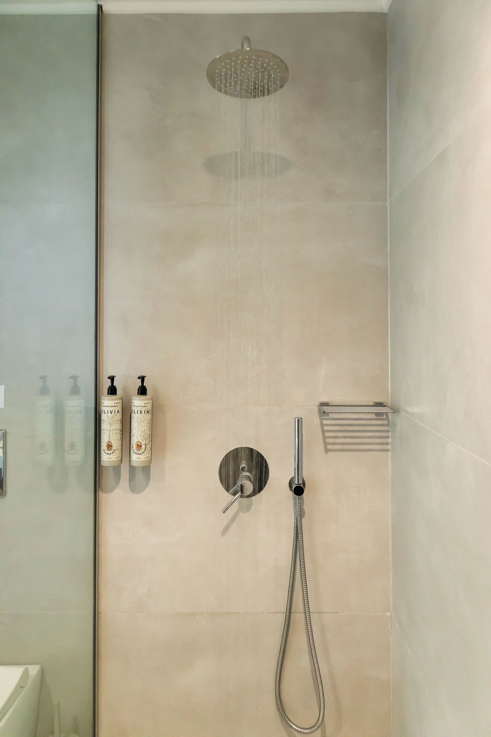 A modern shower area with a rain showerhead, a handheld showerhead, and two bottles of shampoo on the wall.