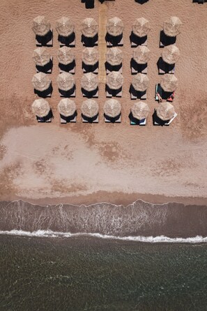An aerial view of a beach with rows of sun loungers and umbrellas, a sandy beach, and a clear view of the ocean. - Batis Aero Beachfront Wellbeing Hotel (Rethymno)