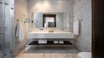 A modern bathroom with a large marble sink, a mirror above it, and a shower area to the left.