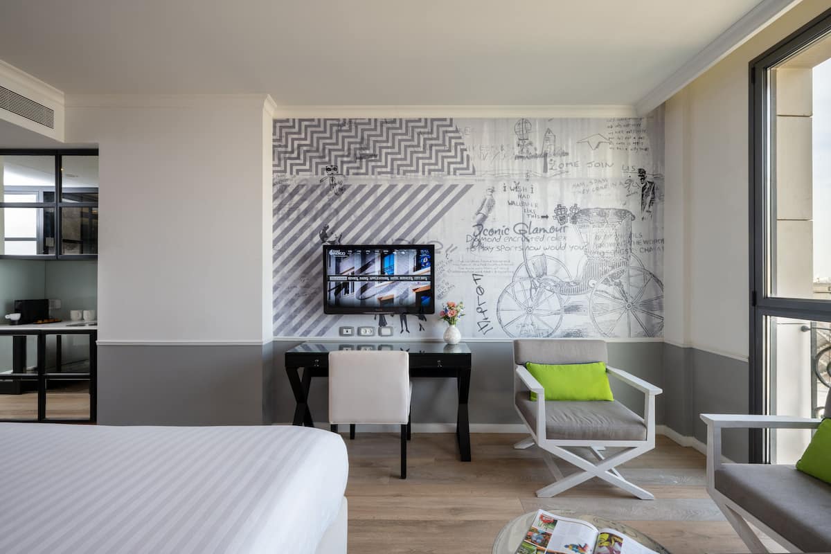 Een moderne hotelkamer met een bed, een bureau met een computer, een stoel en een groot raam.