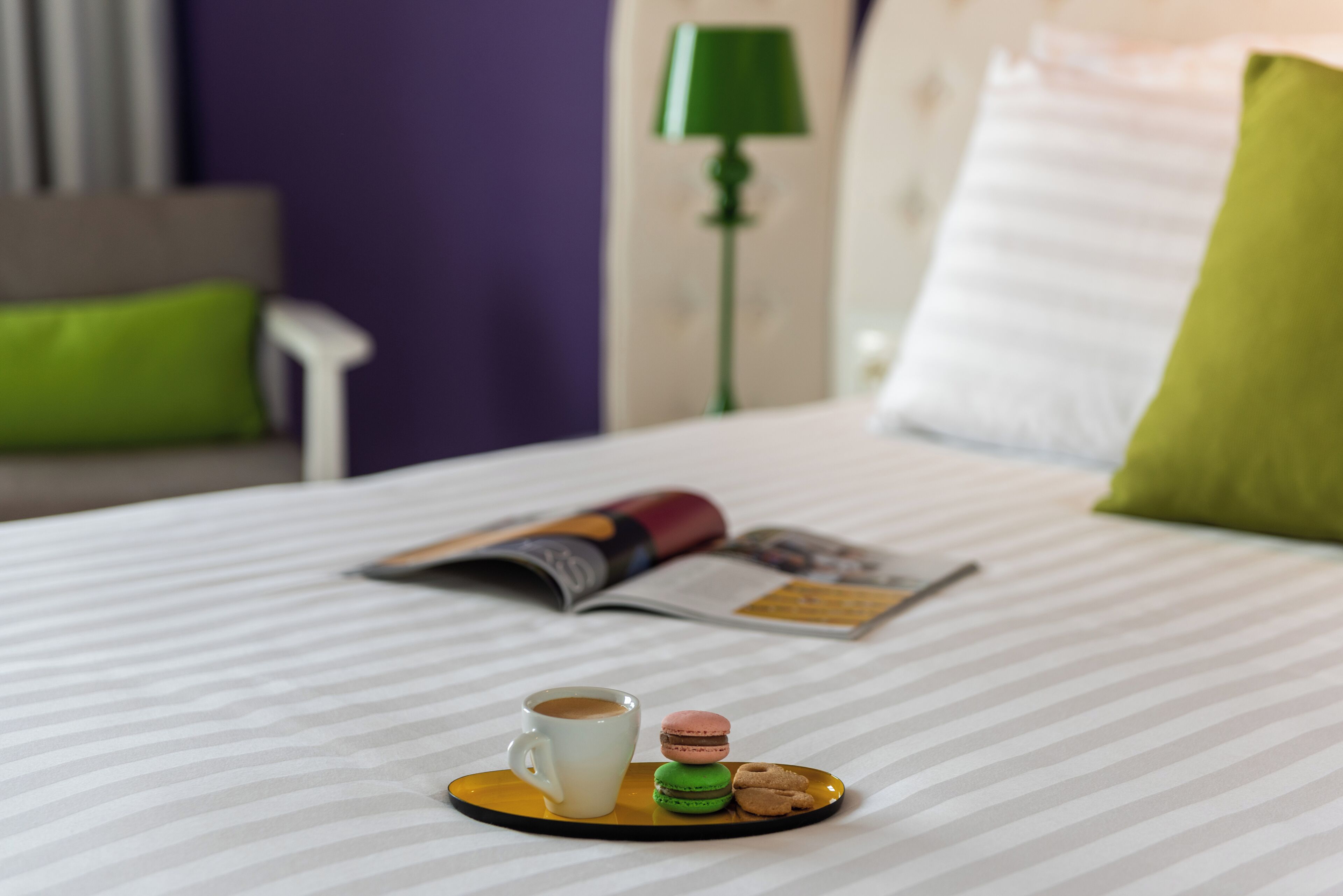 Uma cama bem arrumada com um edredom listrado, um travesseiro verde, um travesseiro branco, um abajur verde e uma revista sobre a cama.