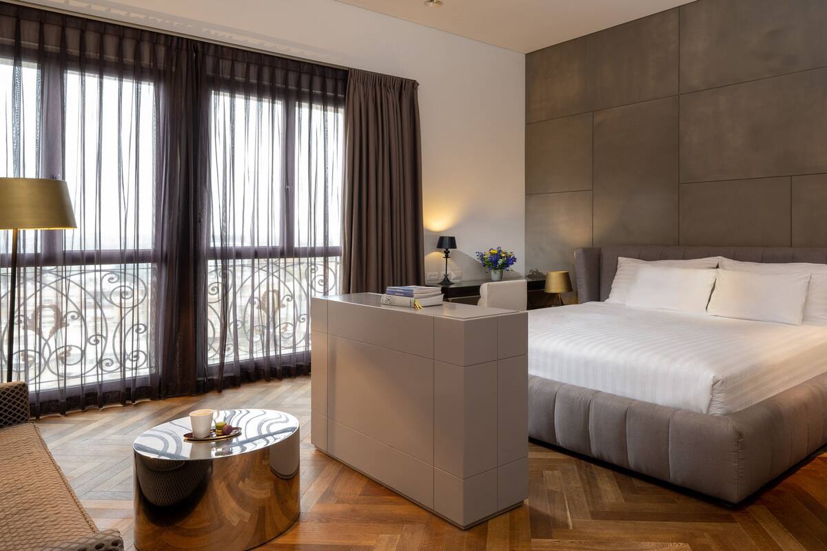 Een moderne hotelkamer met een groot bed, een bureau en uitzicht door dunne gordijnen.