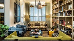 A modern living room with a patterned sofa, a coffee table, and a bookshelf filled with books. - Hotel Indigo Tel Aviv - Diamond District by IHG (Ramat Gan)