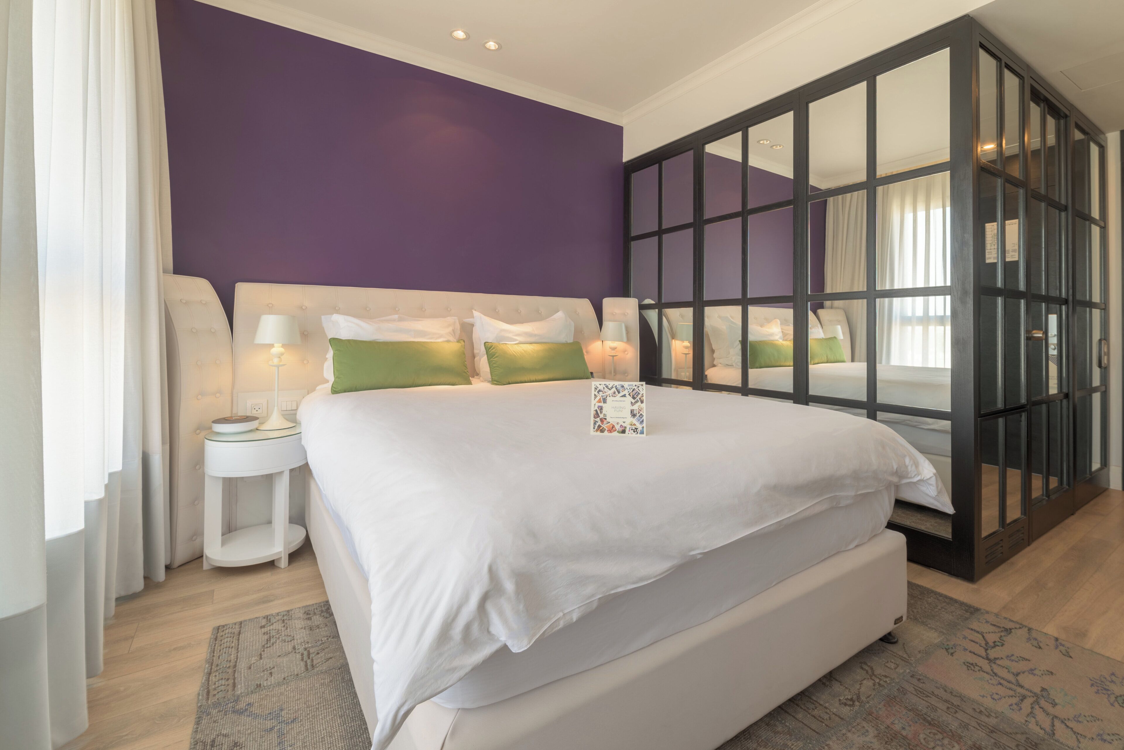 A bedroom with a large bed, a nightstand, a lamp, and a book titled 'Having Fun'.
