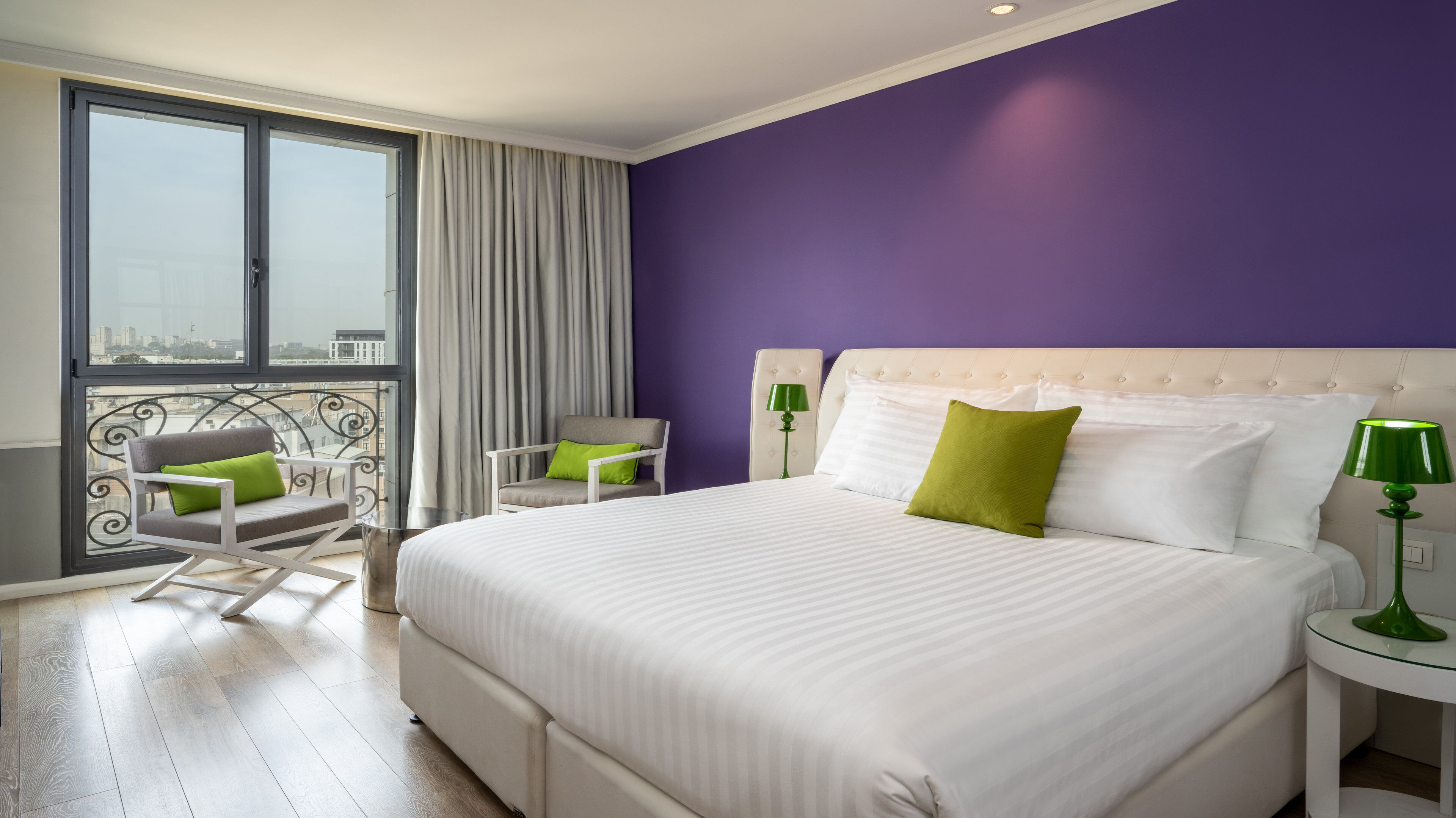 A hotel room with a large bed, a chair, a table, and a view through a window.