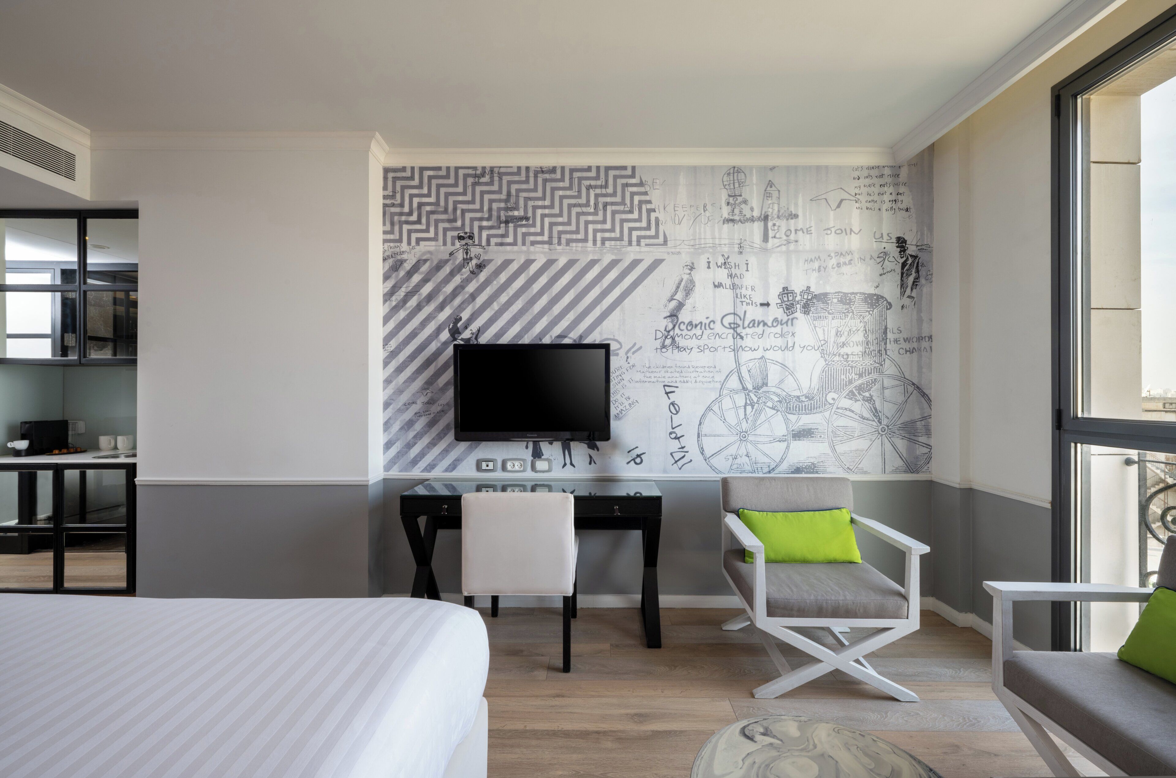 Ein Hotelzimmer mit einem Bett, einem Schreibtisch mit Fernseher, einem Sessel und einem Sofa sowie einem großen Fenster.