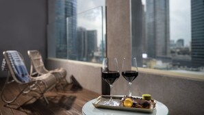 A balcony with two lounge chairs, two wine glasses, and a tray with food and a drink. - Hotel Indigo Tel Aviv - Diamond District by IHG (Ramat Gan)