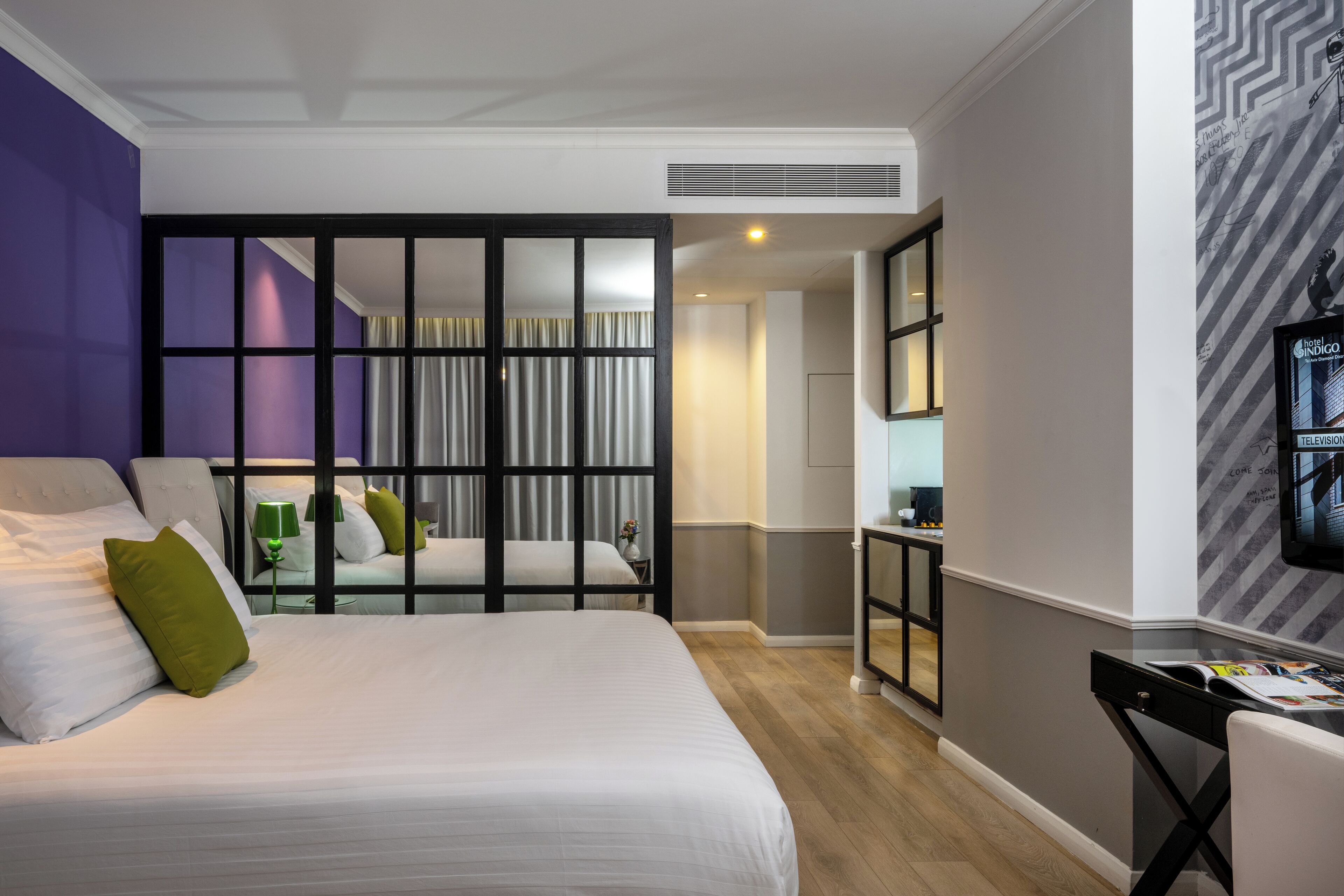 A modern hotel room with a large bed, a desk, and a television.