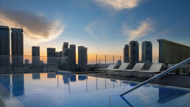 A rooftop infinity pool with city skyline views, lounge chairs, and a modern architectural design. - Hotel Indigo Tel Aviv - Diamond District by IHG (Ramat Gan)