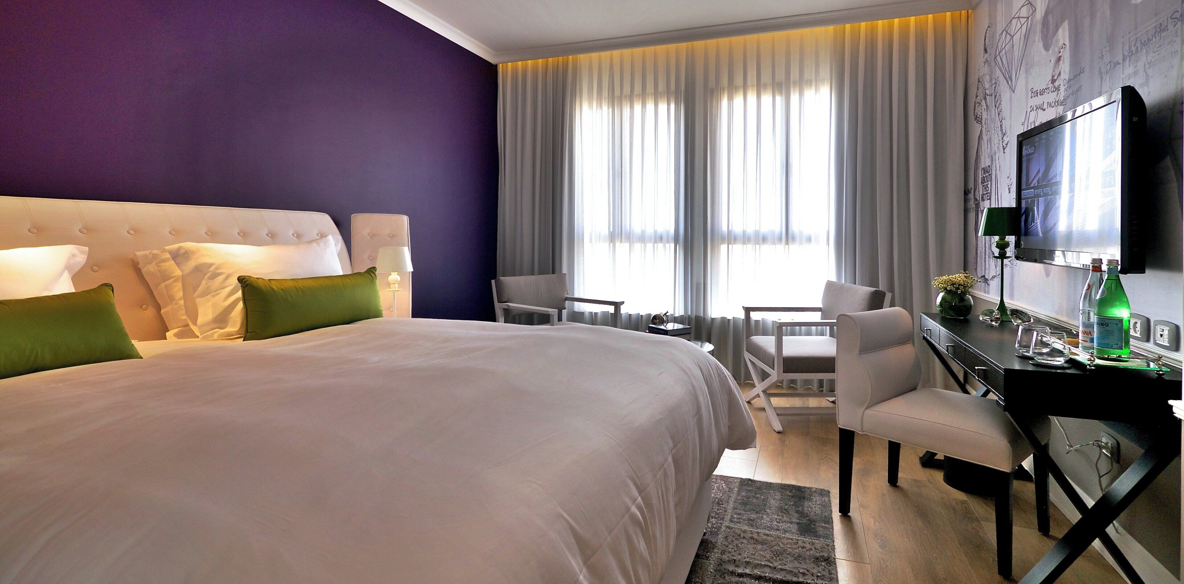 Une chambre d’hôtel avec un grand lit, deux fauteuils, un bureau avec un ordinateur et une télévision.