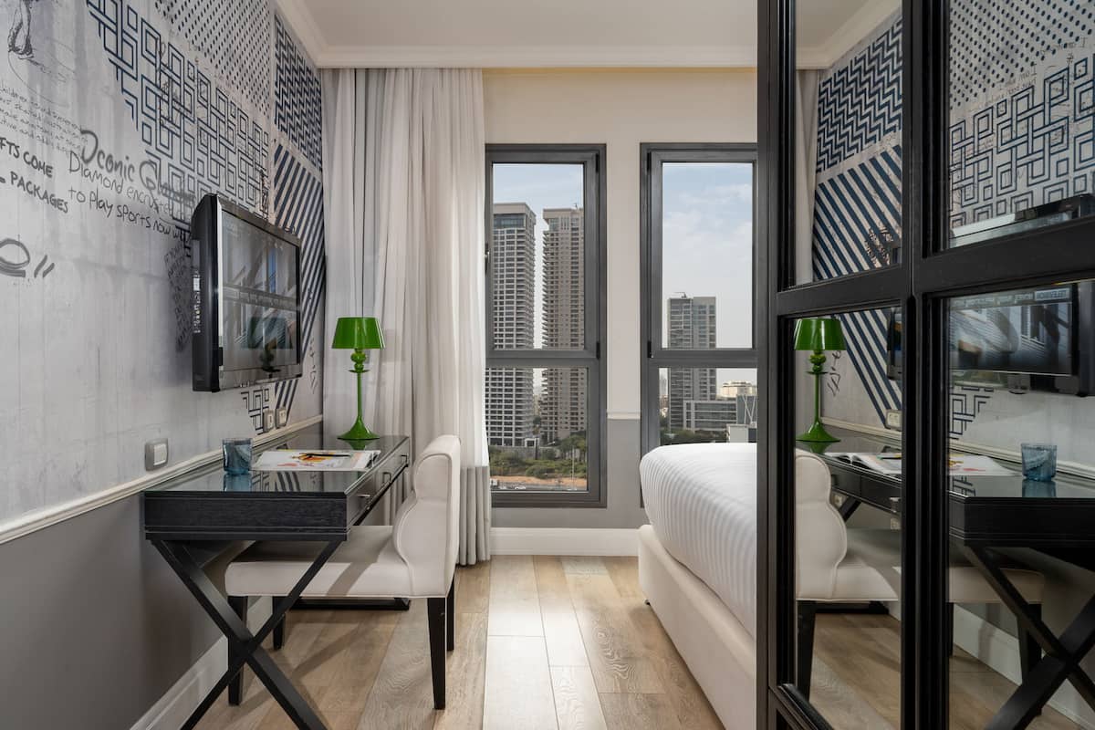 Een moderne hotelkamer met een groot bed, een bureau met stoel, een televisie en een raam met uitzicht op de stad.