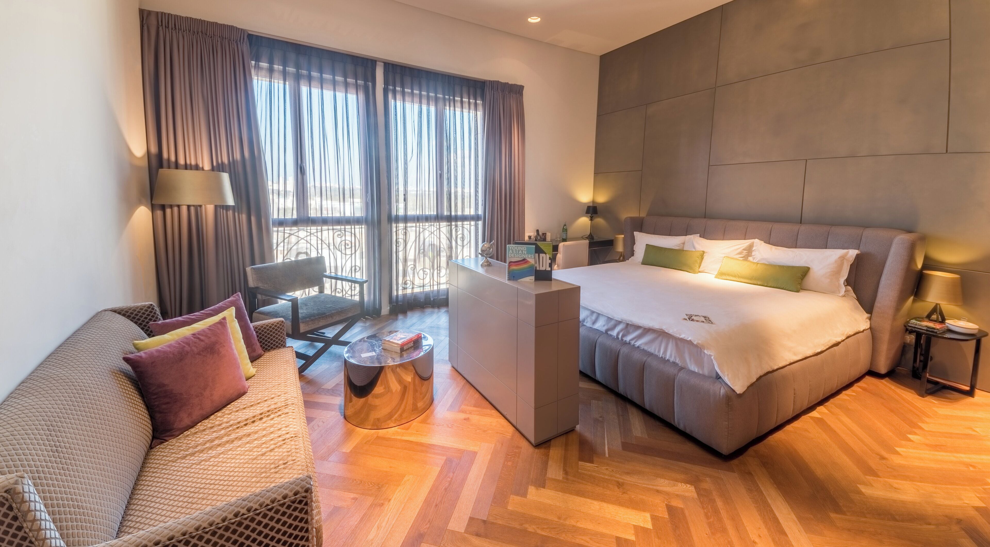 Quarto de hotel moderno com uma cama grande, sofá, escrivaninha e vista para o exterior.