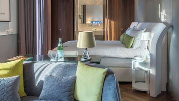 Una habitación de hotel con cama, sofá, mesita de noche, lámpara y vaso de agua.