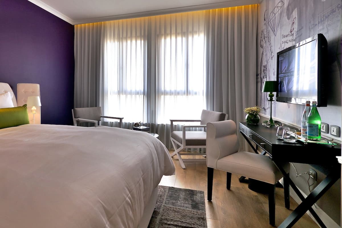 Een hotelkamer met een groot bed, een bureau met stoel, een televisie en een raam met gordijnen.