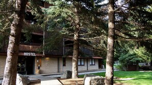 A rustic building labeled 'HOSTEL' with a brick facade, large windows, and a balcony. - The Hostel (Teton Village)