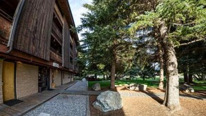 A rustic building with a wooden exterior, a covered outdoor seating area, and a well-maintained garden with trees and gravel paths. - The Hostel (Teton Village)