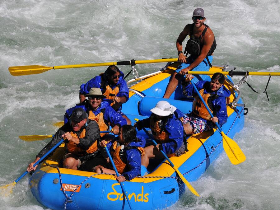 A group of people in a blue and yellow raft with paddles, navigating through white water.