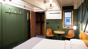 A room with a bed, two chairs, a small table, a window, and an air conditioning unit. - The Hostel (Teton Village)