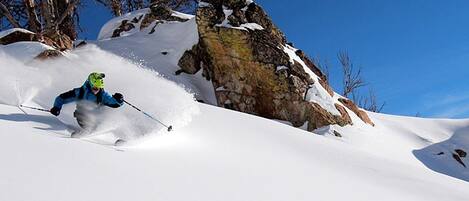 A skier on a snowy slope with rocky outcrops and a clear blue sky.