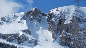 A snow-covered mountain with rocky cliffs and a ski lift cable. - The Hostel (Teton Village)