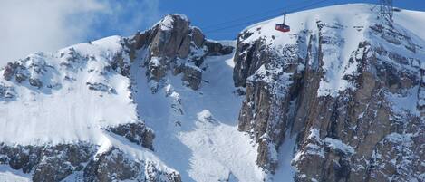 A snow-covered mountain with rocky cliffs and a ski lift cable.