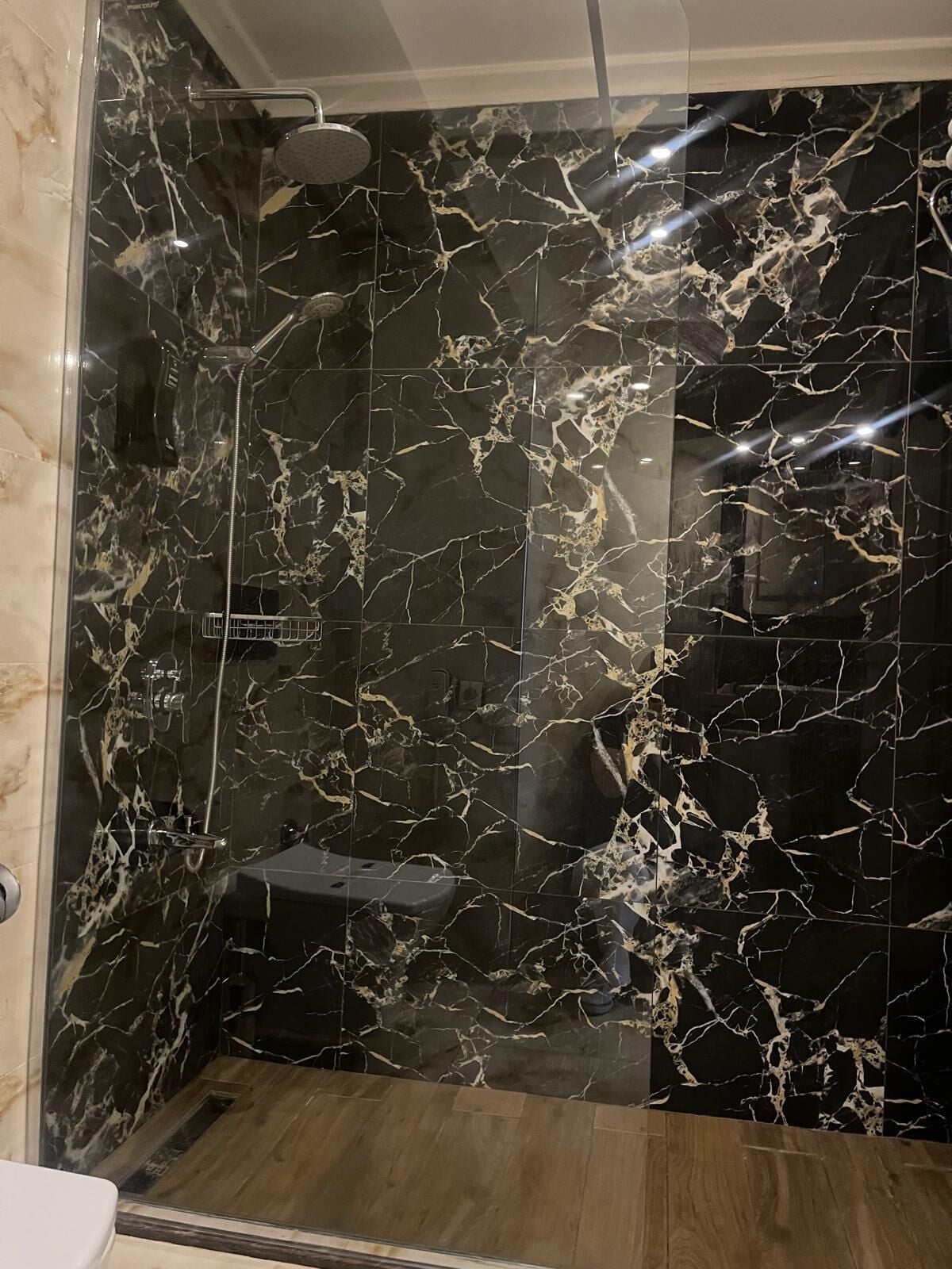 A bathroom with a black marble shower wall, a wooden floor, and a glass shower enclosure.