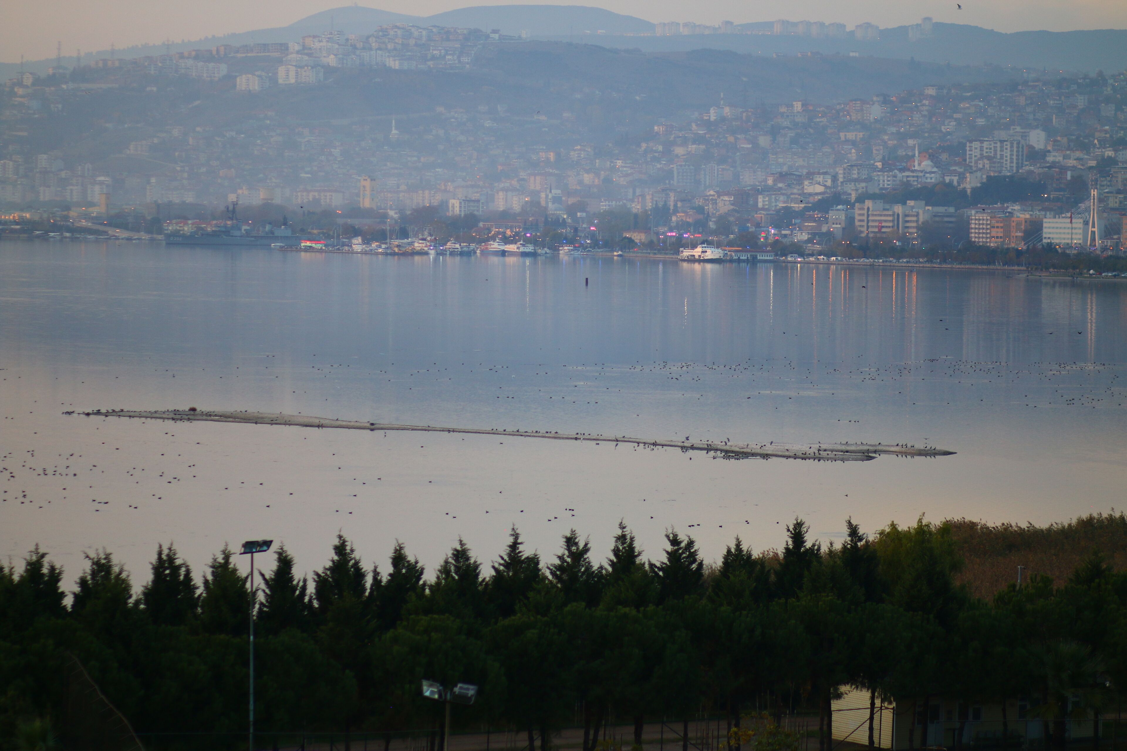 Un paisaje urbano frente al agua, con vista despejada al agua, un puente y una cadena montañosa distante.