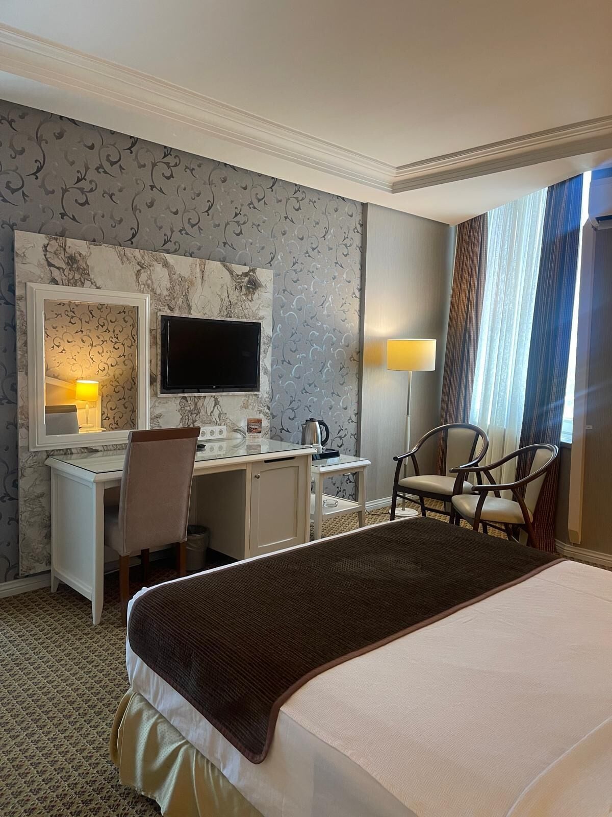 Una habitación de hotel con cama, escritorio, silla, televisión y espejo.