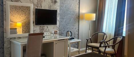 Una habitación de hotel con cama, escritorio, silla, televisión y espejo.