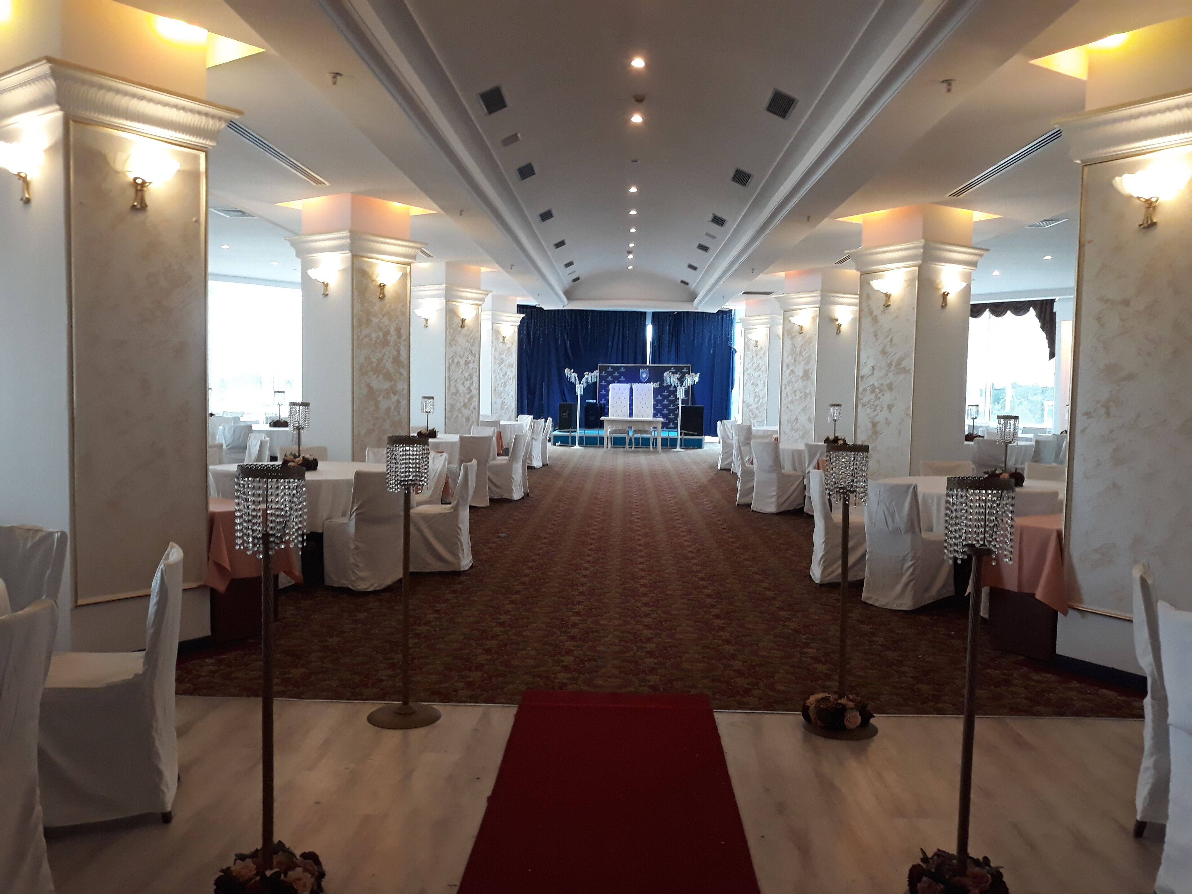 A formal event space with rows of tables and chairs, a red carpet aisle, and a stage with a blue curtain.