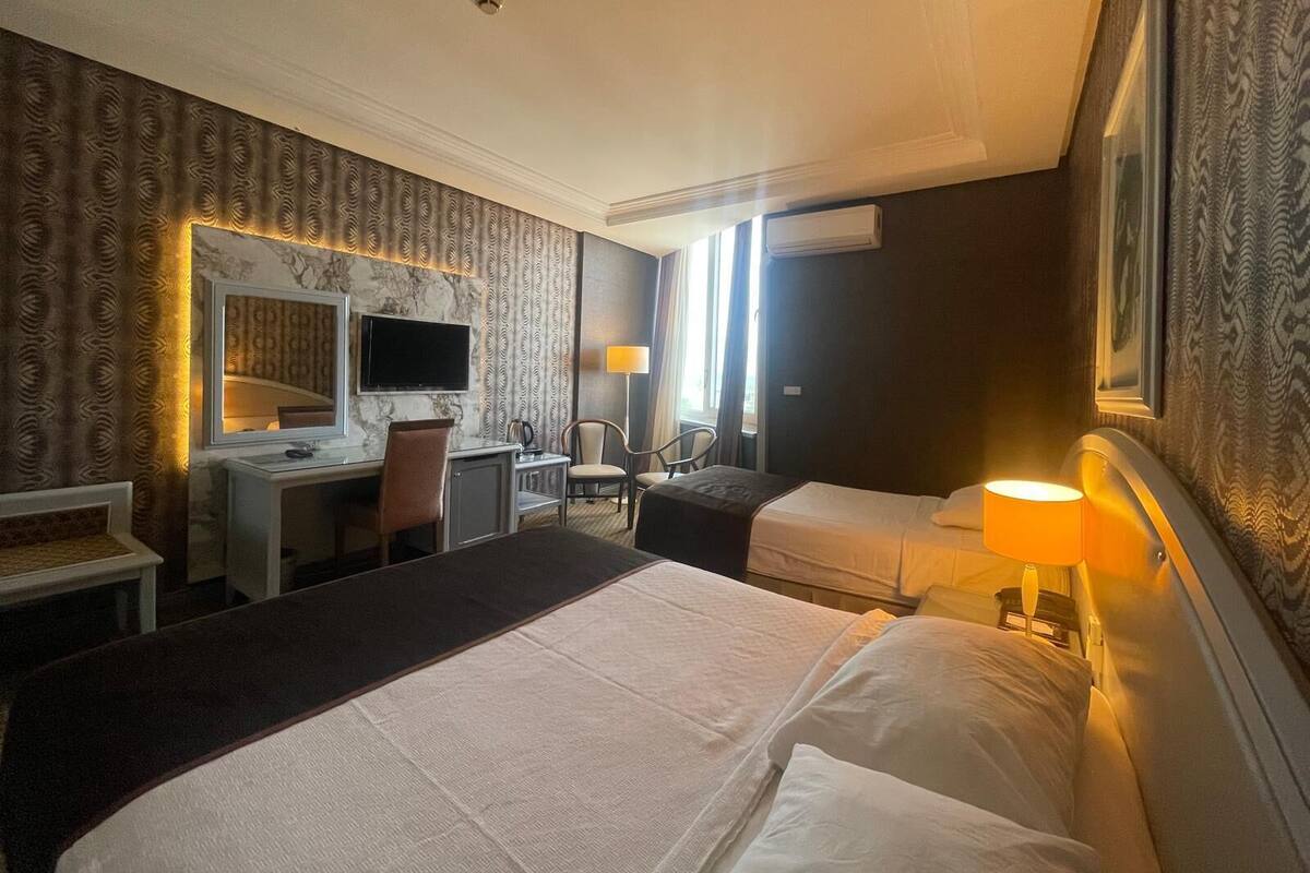 A hotel room with a large bed, a desk with a computer, a chair, and a TV.