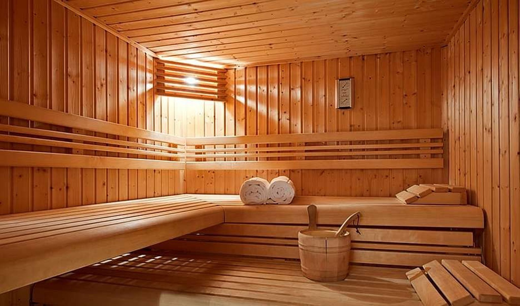 Una sauna con bancos de madera, un balde de madera y un termómetro en la pared.