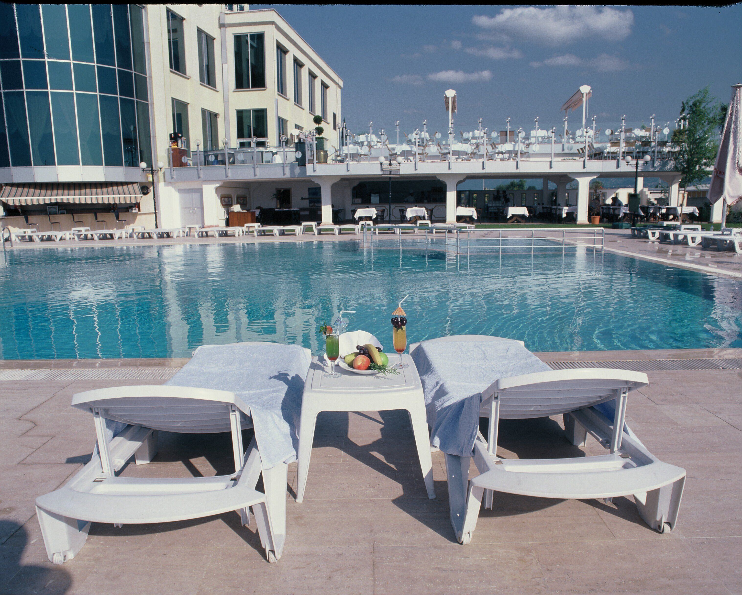 Un espace aménagé au bord de la piscine, avec des chaises longues et une table où sont disposés des fruits et une boisson.