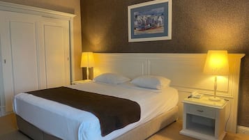 A hotel room with a large bed, two bedside tables with lamps, a painting on the wall, and a door to the left.