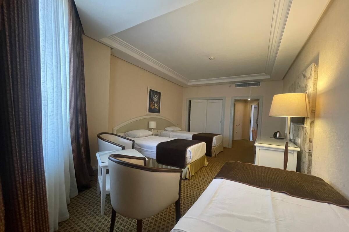 A hotel room with two beds, a desk, a chair, and a lamp.
