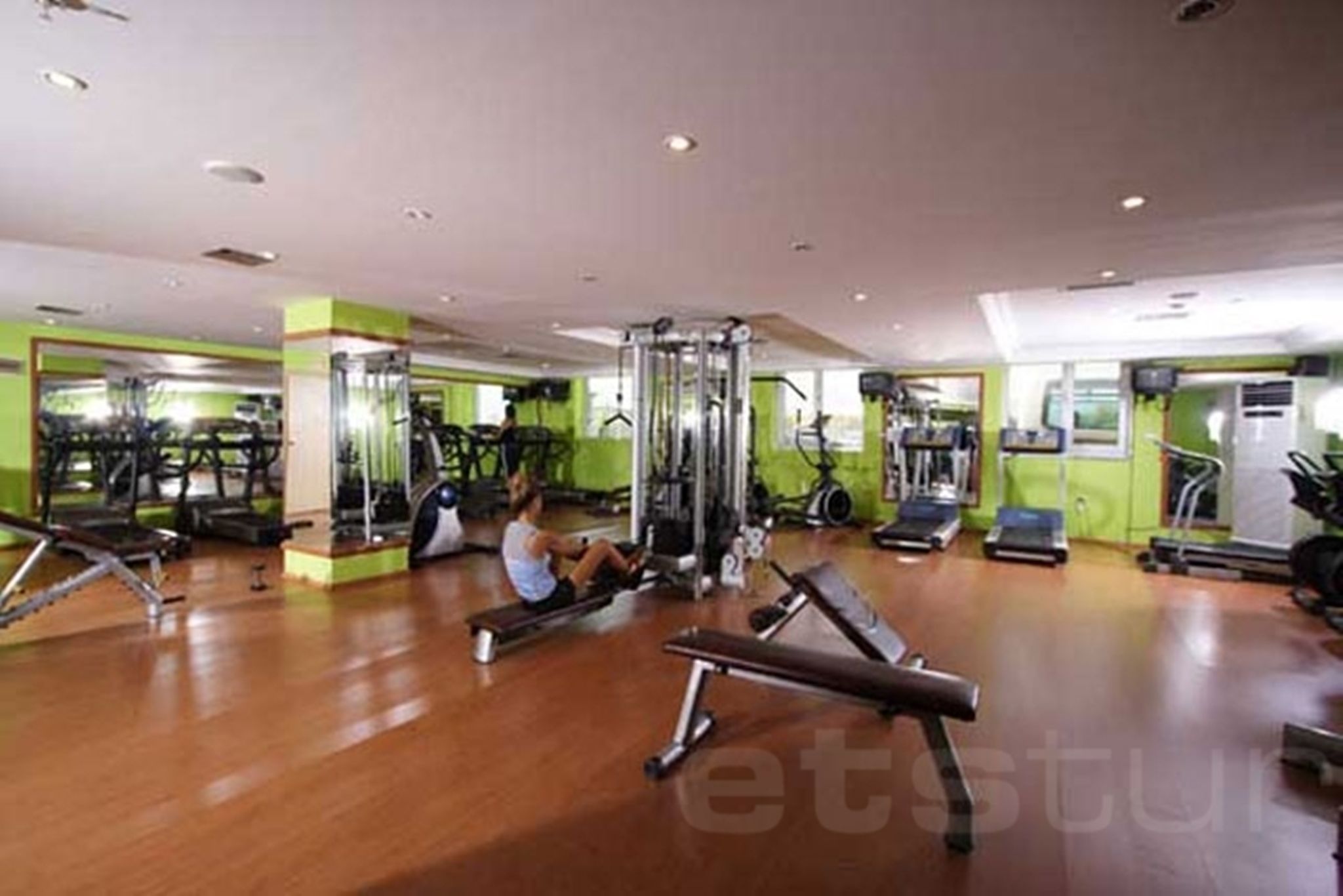 Un gimnasio con equipo de ejercicio, una persona usando una máquina de remo y un espejo grande.