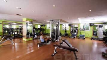 Un gimnasio con equipo de ejercicio, una persona usando una máquina de remo y un espejo grande.