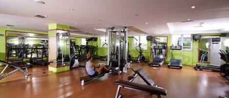 Un gimnasio con equipo de ejercicio, una persona usando una máquina de remo y un espejo grande.