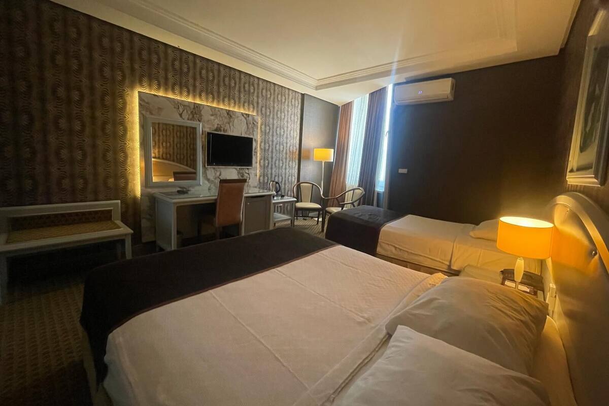 A hotel room with a large bed, a desk with a chair, a television, and a window with curtains.