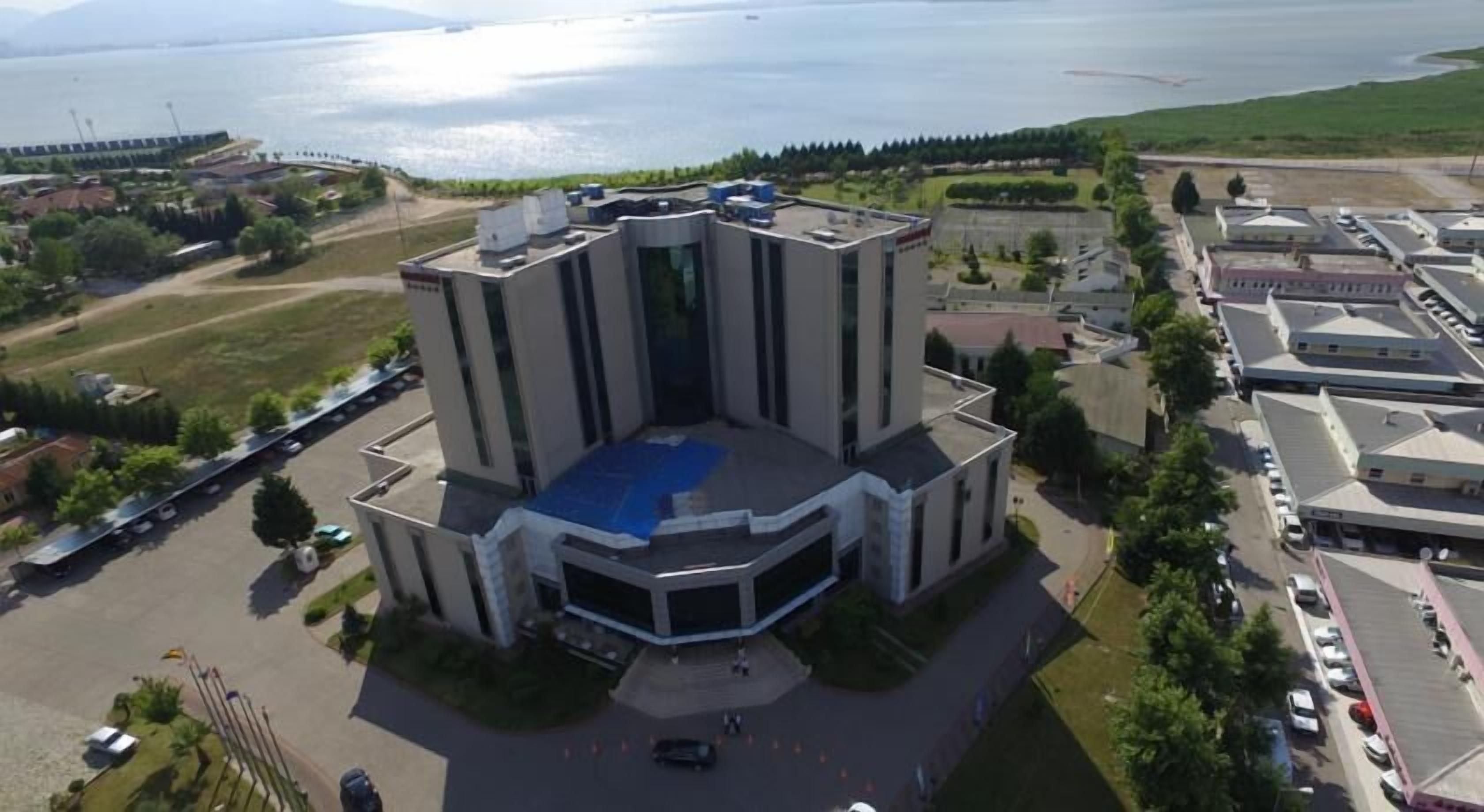 Un grand bâtiment moderne doté d’une cour intérieure et d’un toit bleu, entouré d’un parking et d’espaces verts.