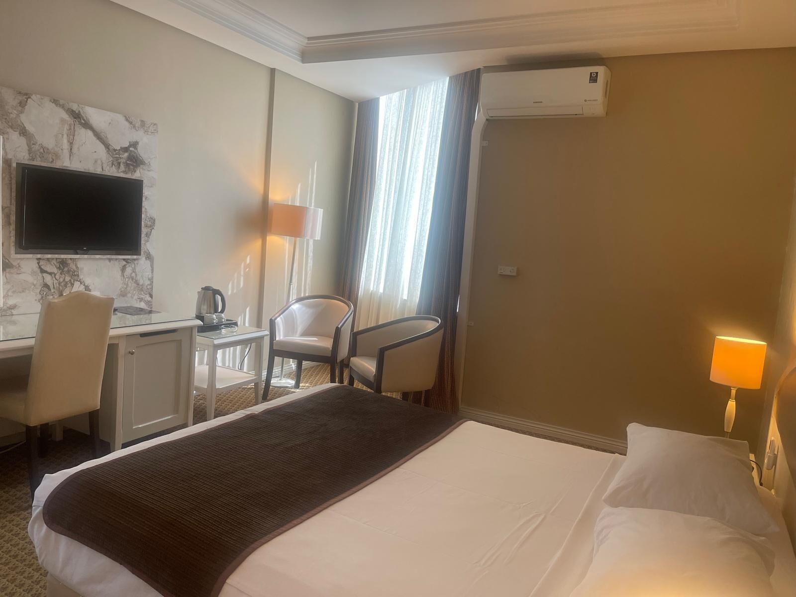 Habitación de hotel con cama, escritorio, silla, televisión y aire acondicionado.