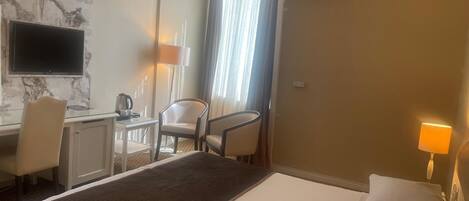 Habitación de hotel con cama, escritorio, silla, televisión y aire acondicionado.