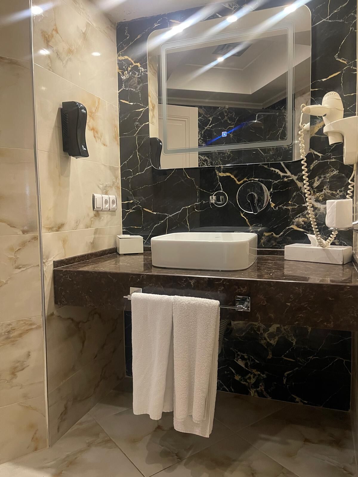 Un baño moderno con tocador de mármol, un espejo grande, un secador de pelo y un perchero para toallas.