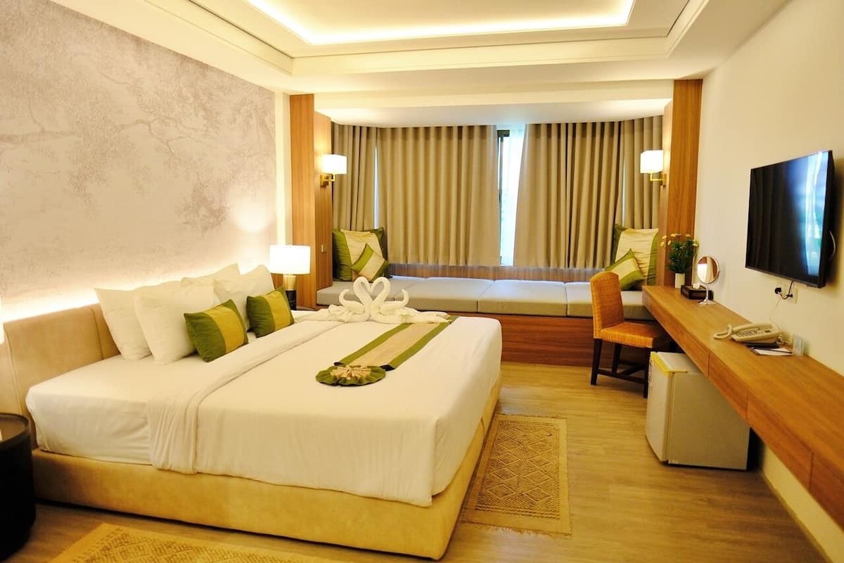 A hotel room with a large bed, a desk, a chair, a television, and a window with curtains.