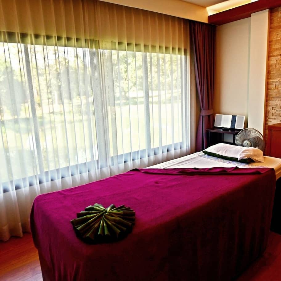 A massage table with a purple cover, a fan, a laptop, and a mirror on a brick wall.