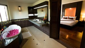 A modern bathroom with a bathtub filled with rose petals, a large mirror, and a separate bedroom with a bed and nightstand. - Mae Jo Golf Club & Resort (San Sai)