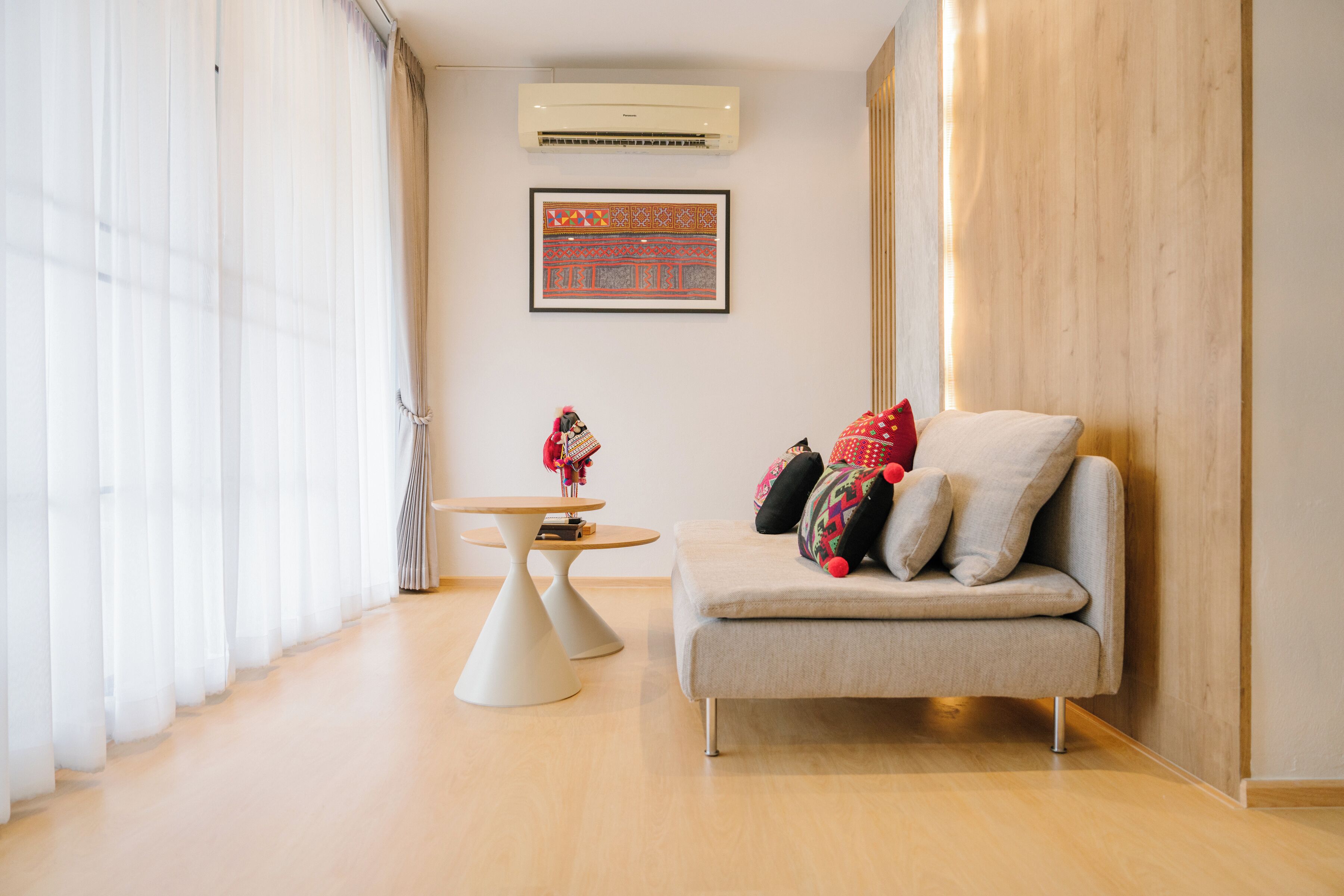 A modern living room with a sofa, a small round table, and a wall-mounted air conditioner.