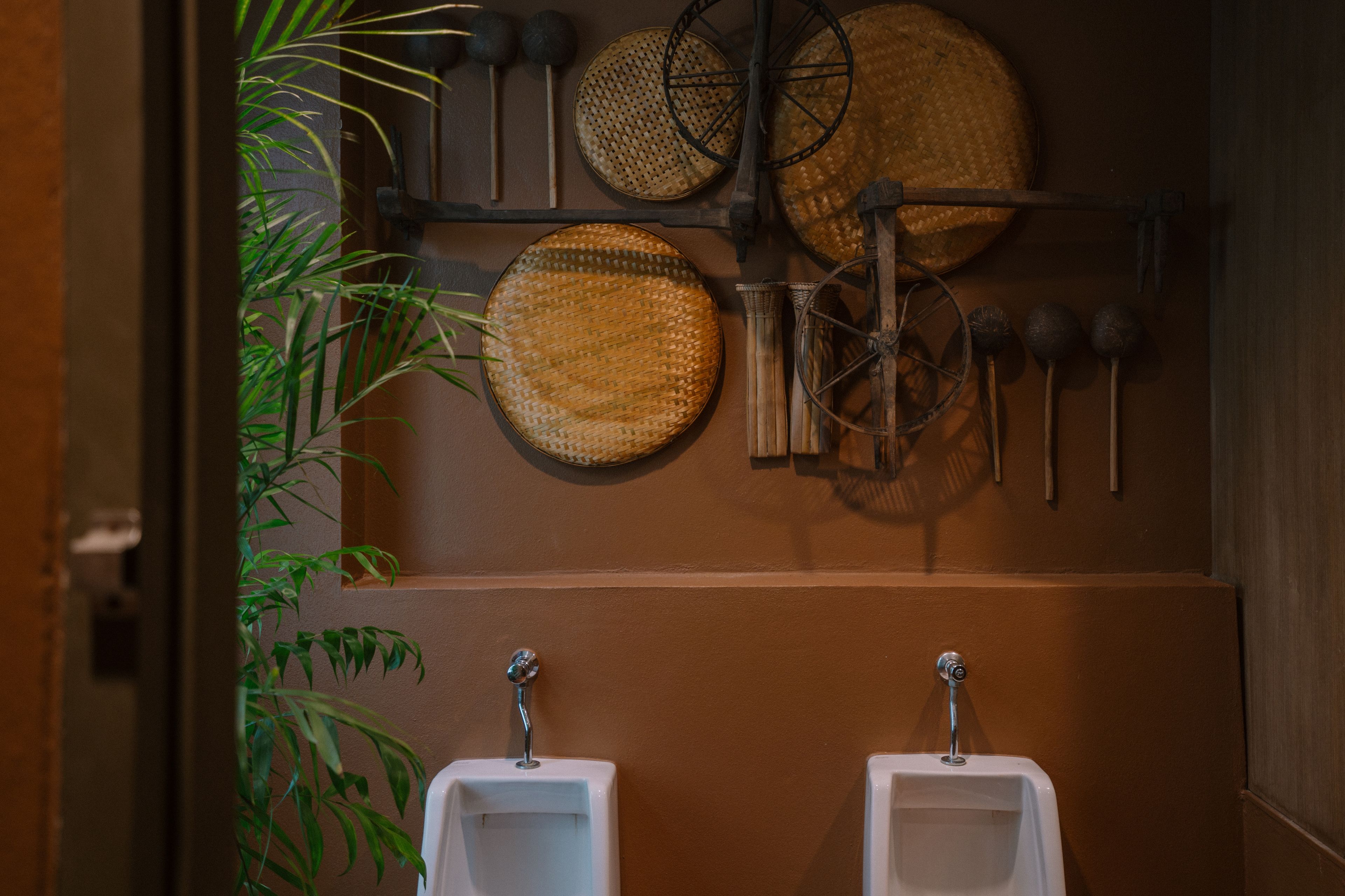 Un baño con dos orinales, un perchero con sombreros en la pared y una planta en maceta.