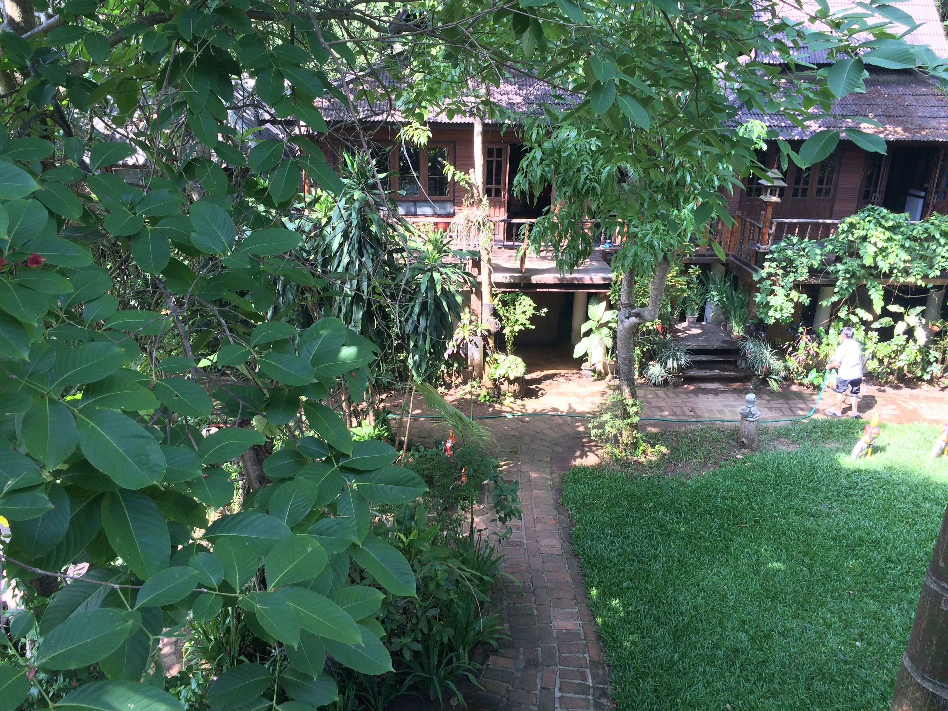 A traditional wooden house with a thatched roof, surrounded by lush greenery and a well-maintained garden.