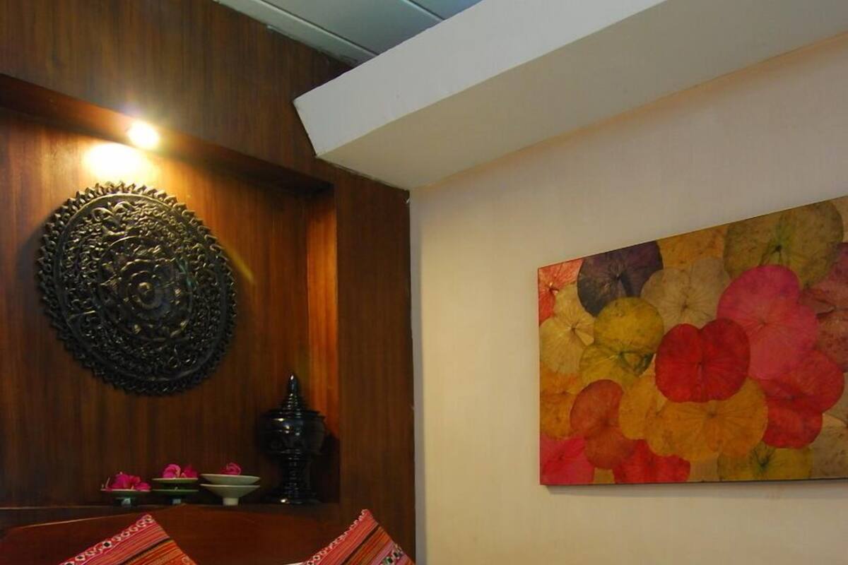 A hotel room with a wooden headboard, a bed with white and red bedding, a floral painting on the wall, and a small table with a decorative item.